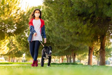 Korumalı maske takan bir kadın, Corona virüsü salgını yüzünden dışarıda köpekle birlikte yürüyor.