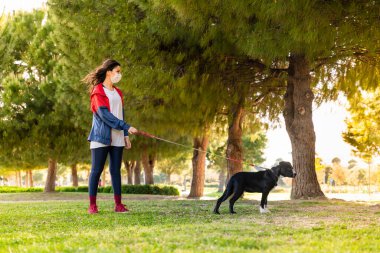 Korumalı maske takan bir kadın, Corona virüsü salgını yüzünden dışarıda köpekle birlikte yürüyor.
