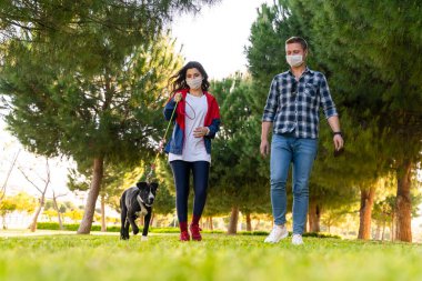 Korumalı maske takan genç bir çift, Corona virüsü salgını yüzünden dışarıda köpekle birlikte yürüyorlar.