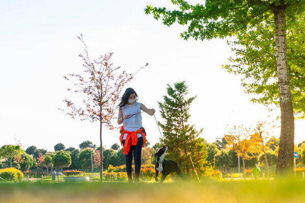 woman wearing a protective mask is walking alone with a dog outdoors because of the corona virus pandemic covid-19