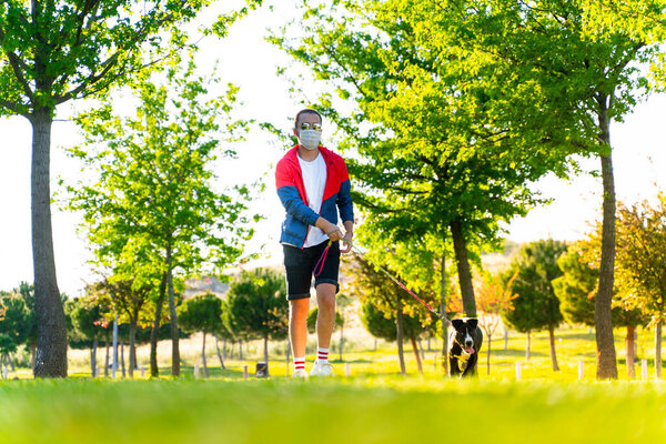 man wearing a protective mask is walking alone with a dog outdoors because of the corona virus pandemic covid-19