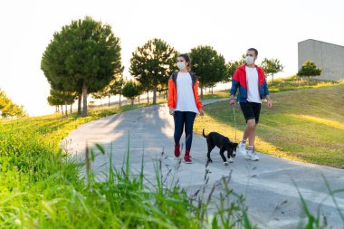Korumalı maske takan genç bir çift, Corona virüsü salgını yüzünden dışarıda köpekle birlikte yürüyorlar.