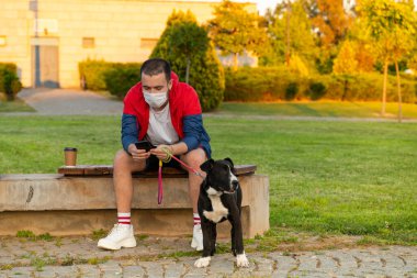 Parkta köpekle oturan ve telefonu kullanan bir adam.