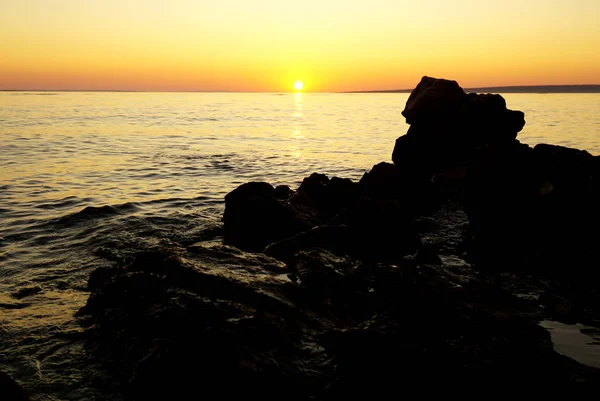 Groot rots silhouet aan de zeekust bij oranje zonsondergang — Stockfoto