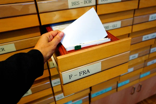 Eski bir katalog üzerinde ahşap çekmece kutusu ve katalog fişi tutan bir el.