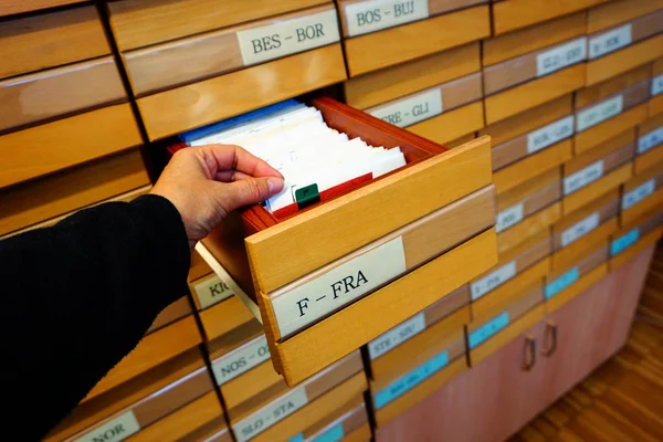 Mão que contém documentos de uma gaveta aberta em um catálogo de biblioteca antiga de arquivo de madeira — Fotografia de Stock