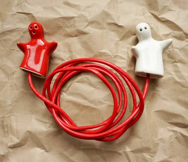Připojení nebo odpojení jako koncept. Dvojice červenobílých keramických figurek spojených s červeným drátem — Stock fotografie