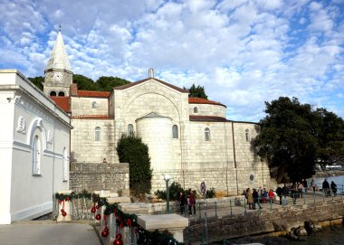 Hırvatistan 'ın Opatija kasabasındaki Aziz Jacob Kilisesi ve güzel bir Aziz Sylvester gününde gezinti alanında yürüyen insanlar.