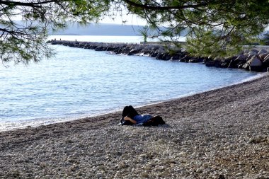 Güneşli bir kış gününde kumsalda güneşlenen bir kadın.