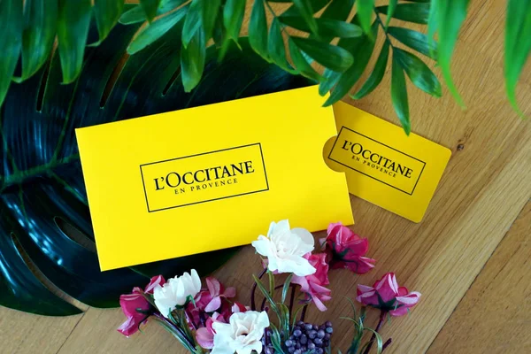 Loccitane en Provence gift card gialla per lo shopping cosmetico naturale e biologico per la cura della pelle, dei capelli e del corpo sullo sfondo in legno decorato con fiori — Foto Stock