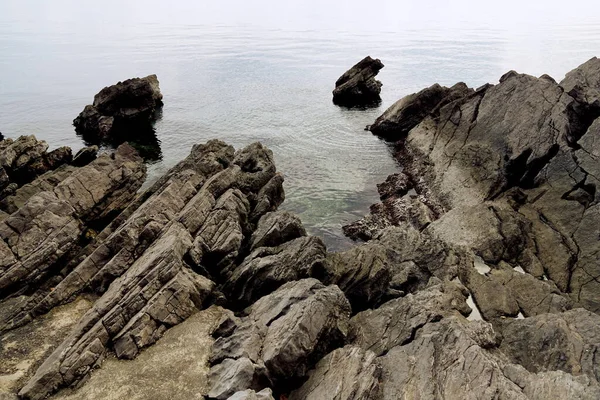 Острые каменистые камни при входе в море в сероватый облачный день — стоковое фото