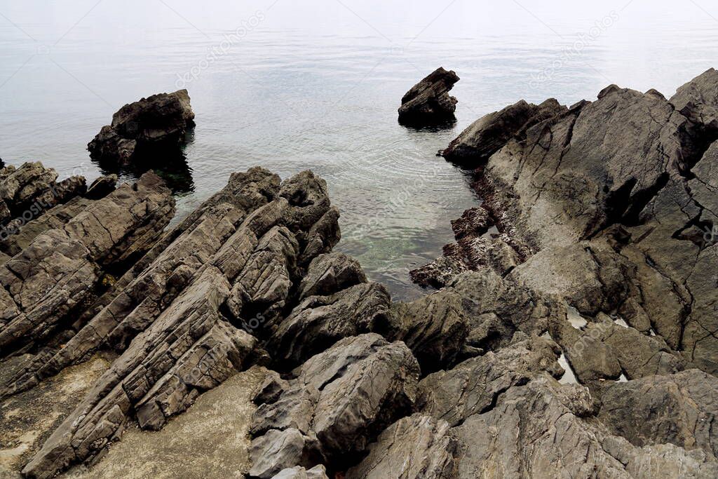 Sharp rocky stones upon entering the sea on the grayish cloudy day