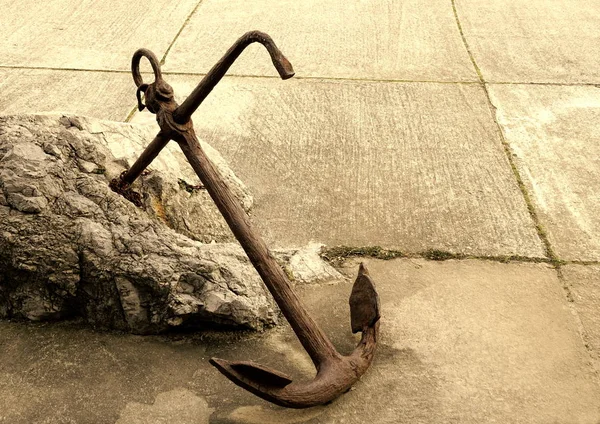 Rusted iron anchor not in use, discarded and leaning against stone Stock Picture