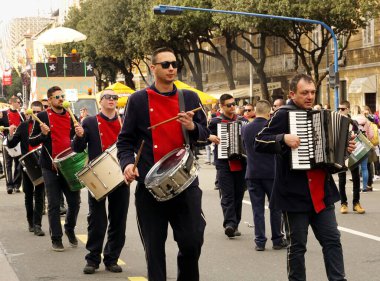 Rijeka, Hırvatistan, 23 Şubat 2020. Akordiyoncular ve yakışıklı genç oğlanlar kırmızı ve siyah üniformalı davulcular karnaval alayında yürüyor ve davulları çalıyorlar.