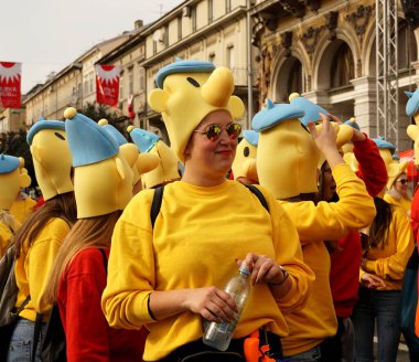 Sarı tişörtlü ve gözlüklü neşeli genç bir kadın karnavalda, Pat ve Mat animasyon karakterleriyle maskeli.