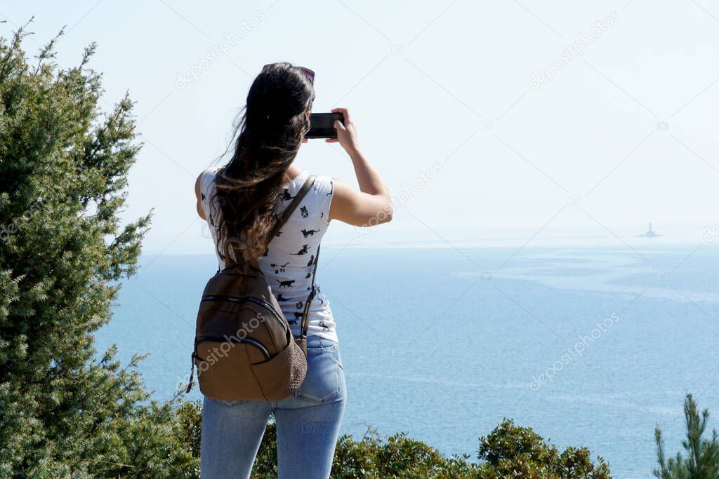 Young girl photographing a beautiful unpolluted nature and open deep sea, with a smartphone