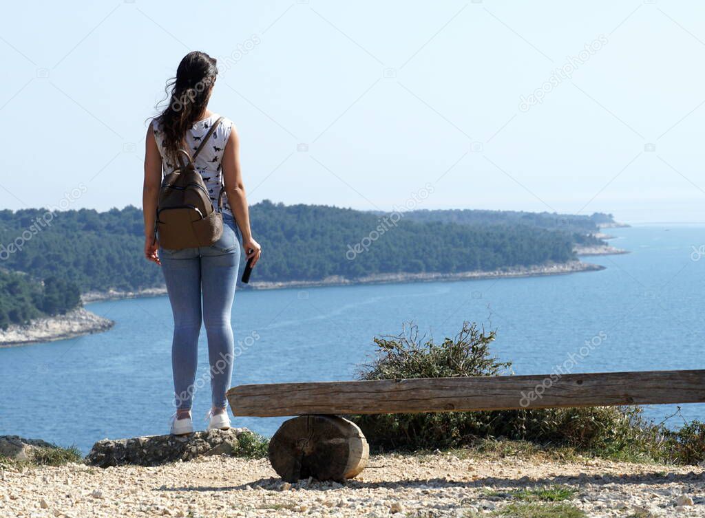 Young girl standing on a high cliff and looking out over the open blue sea