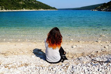 Turkuaz ve mavi gölde güzel bir doğa ve düşünen, rahatlatan ve denizin tadını çıkaran genç bir kadın.