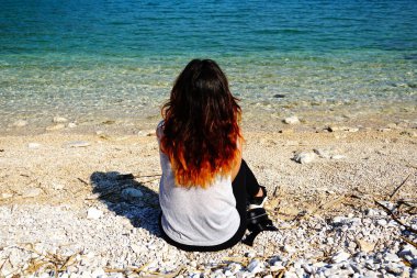 Milenyum kadını çakıl taşı sahilinde oturuyor ve güzel doğada yürüdükten sonra meditasyon yapıyor.