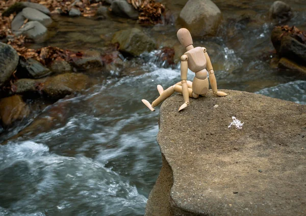 Eklemli küçük adam bir dağ nehrinin üstündeki bir taşın üzerinde oturuyor.
