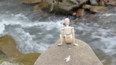 Eklemli küçük adam bir dağ nehrinin üstündeki bir taşın üzerinde oturuyor.