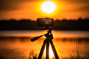 Akıllı telefon gölde günbatımı videosu çekiyor.