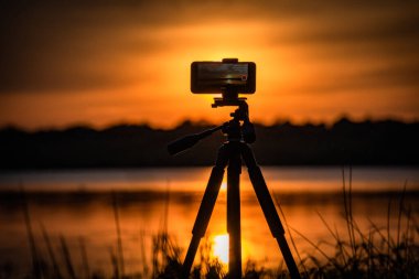 Akıllı telefon gölde günbatımı videosu çekiyor.