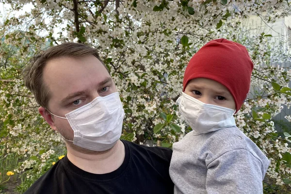 Tıbbi maskeli küçük bir çocuk bir adama sarılıyor. Babası oğlunu tutuyor. İkisi de koruyucu maske takıyor. Virüs koruma konsepti..