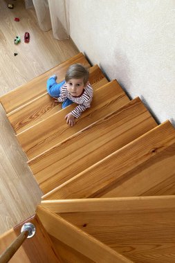 Cute smiling young boy sitting on stairs on the second floor, top view clipart