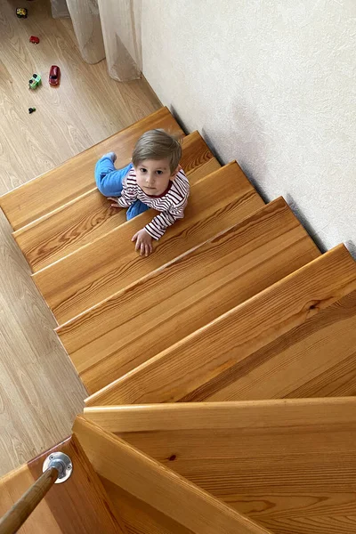 İkinci kattaki merdivenlerde oturan sevimli, gülümseyen genç çocuk.