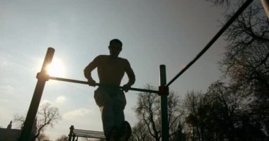 Genç adam güzel bir havada yatay çubukta çekiş yapıyor.