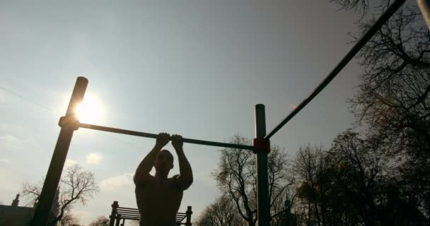 Un jeune homme fait des pull-ups avec une poignée étroite sur la barre horizontale par beau temps 4K — Video