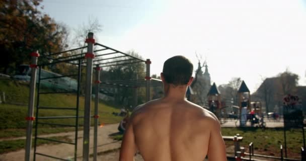 A young man is walking to the sports area and pulling up on the bar in sunny weather 4K — Stock Footage A young man is walking to the sports area and pulling up on the bar in sunny weather 4K Royalty Free Stock Footage