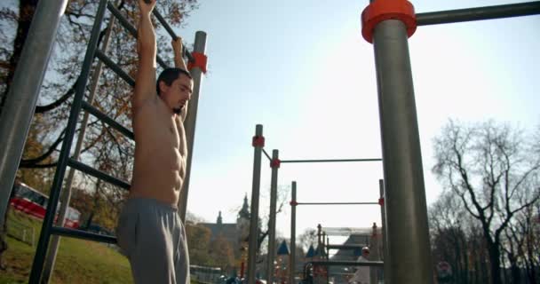 Un hombre está colgando en la escalera y levantando las piernas con buen tiempo 4K — Vídeo de stock