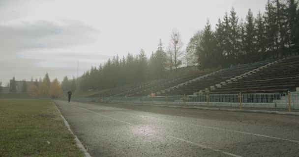 Atlet, sisli sonbahar havasında sabah stadyumun etrafında koşuyor. — Stok video