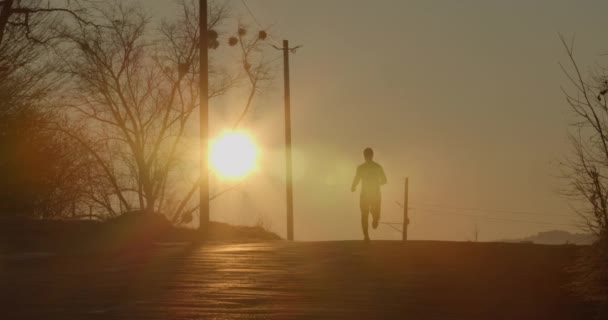 Der Mann rennt im Morgengrauen auf der Straße den Berg hinunter. Kaltes Wetter. 4K . — Stockvideo