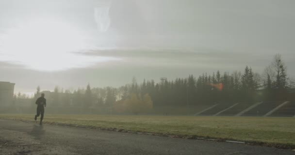 Спортсмен бегает на стадионе утром в туманную осеннюю погоду 4К — стоковое видео