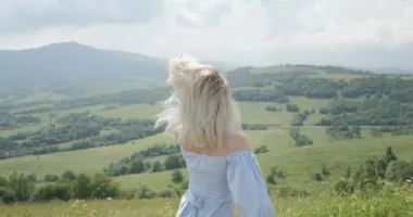 Güneş gözlüklü güzel bir kız gülümsüyor ve dağlara doğru dönüyor. Güneşli bir gün. Arka planda güzel dağlar 4K