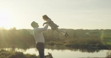 Genç bir baba, küçük kızını kollarına atıyor. Sonbaharda yürüyüşe çıkan bir aile. 4K