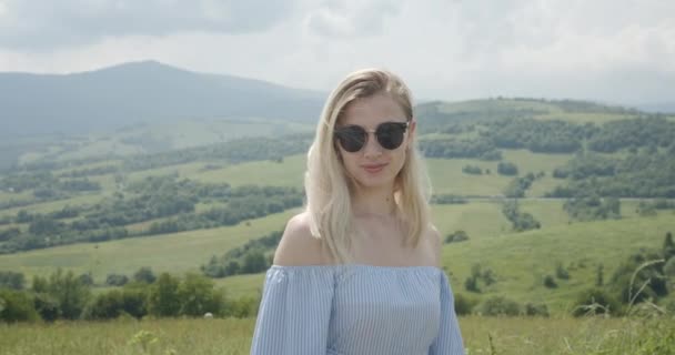 Gyönyörű lány napszemüvegben mosolyog. Napsütéses nap. Gyönyörű hegyek a háttérben 4K — Stock videók