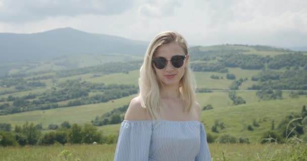 Hermosa chica en gafas de sol está sonriendo. Día soleado. Hermosas montañas en el fondo 4K — Vídeo de stock