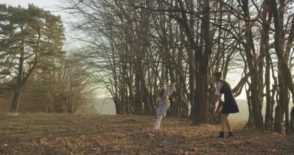 Eine junge Mutter wirft mit ihrer kleinen Tochter Herbstblätter. Familie beim Spaziergang im herbstlichen Wald. 4K — Stockvideo