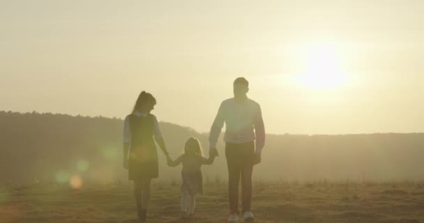 Joyeux jeune famille avec bébé marche dans le champ. Mère, père et petite fille apprécient la nature ensemble à l'extérieur. 4K — Video