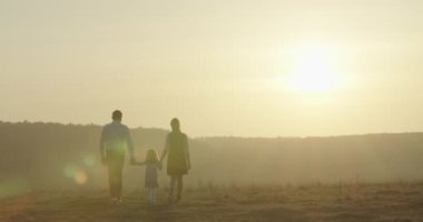 Mutlu genç aile tarlada yürüyor. Anne, baba ve küçük kız birlikte doğanın tadını çıkarıyorlar. 4K