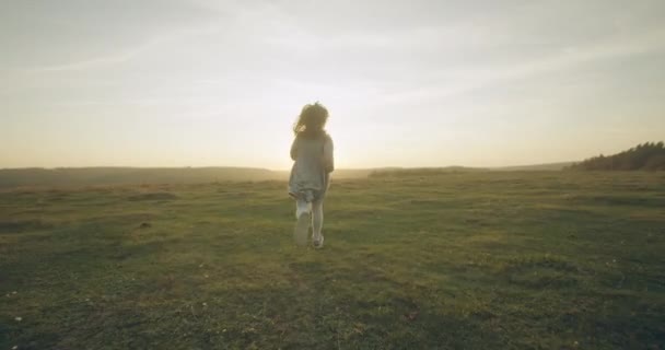 Une petite fille court à travers le champ d'automne sur fond de soleil. Jeune famille en promenade. 4K — Video
