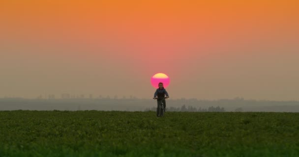 Ein Junge fährt bei Sonnenuntergang mit dem Fahrrad auf einem Gehweg. Filmaufnahmen von hinten. 4K — Stockvideo