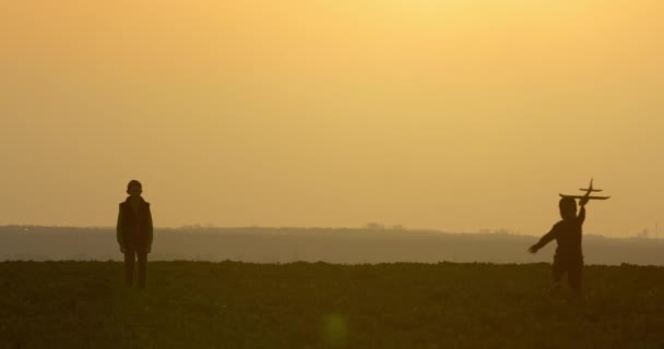 Um rapazinho a correr para o irmão com um avião nas mãos. Pôr do sol. 4K — Vídeo de Stock