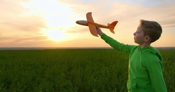 Un garçon avec un avion jouet dans ses mains traverse le champ. Promenade nature. Coucher de soleil. 4K 