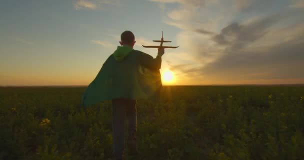 Pojken springer över fältet och skjuter upp planet i skyn. Solnedgång. 4K — Stockvideo