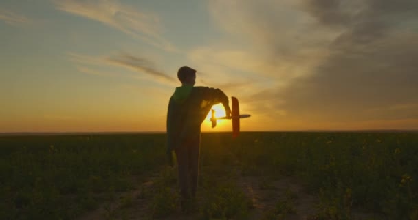 Een jongen staat op het veld en speelt met een vliegtuig. Zonsondergang. 4K — Stockvideo